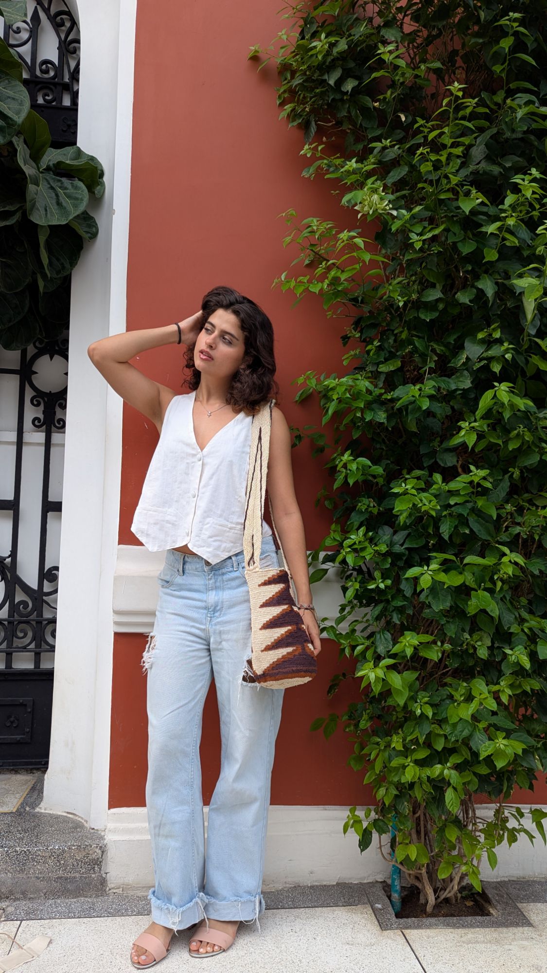 Woman wearing a sleeveless white top and ripped light blue jeans, carrying a handmade Indigenous mochila tote bag with a  triangle  pattern stacked on top of each other, styled for everyday sustainable fashion and casual streetwear.