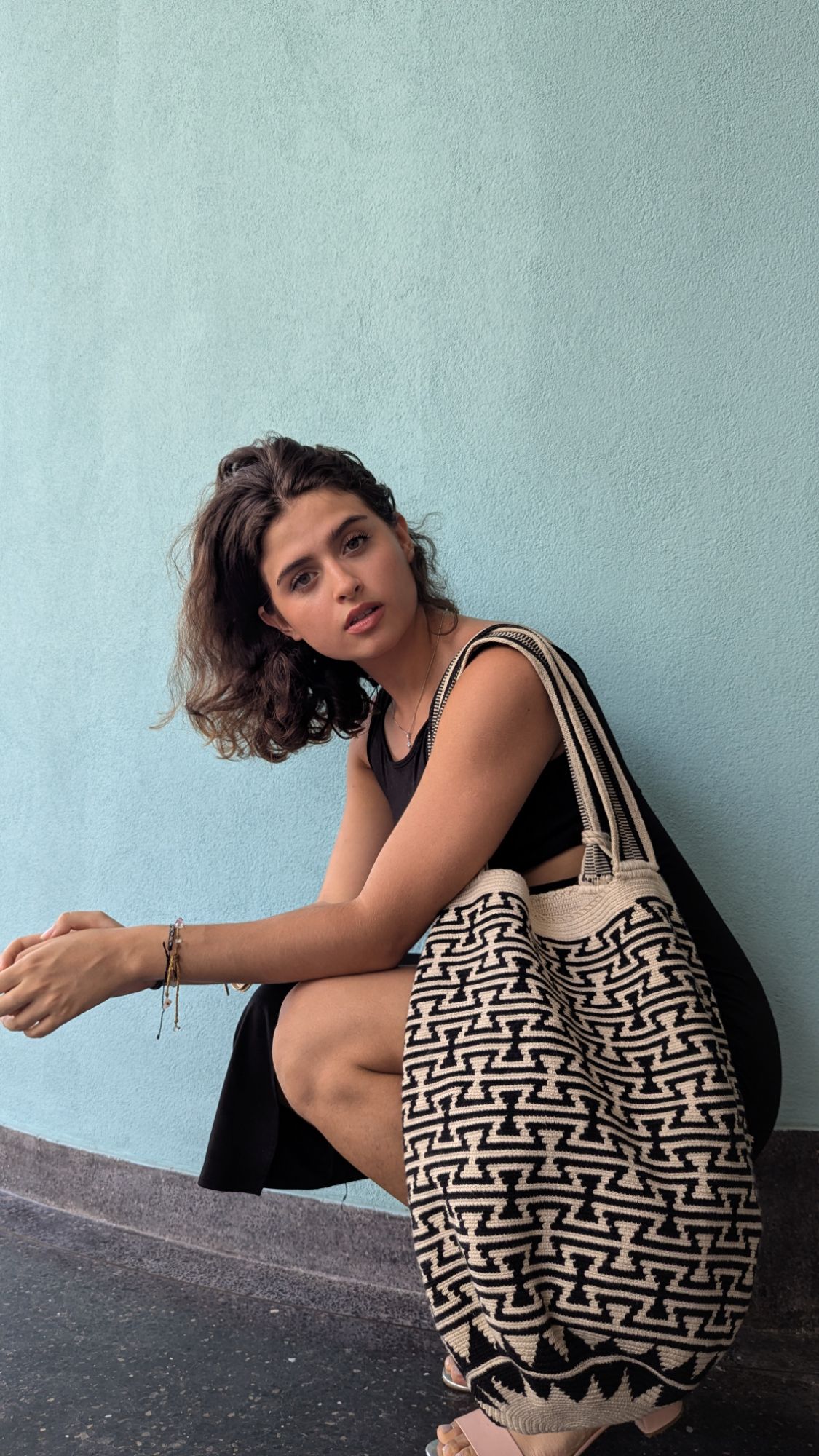 Woman in black dress holding a Wayuu mochila tote bag with bold Indigenous designs, styled for elegant ethical fashion in the city.