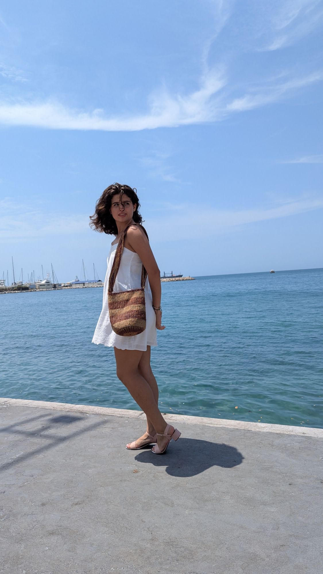 Woman by the sea wearing a white dress and holding a handmade Kogui mochila bag, styled as a boho beach shoulder bag for ethical fashion.